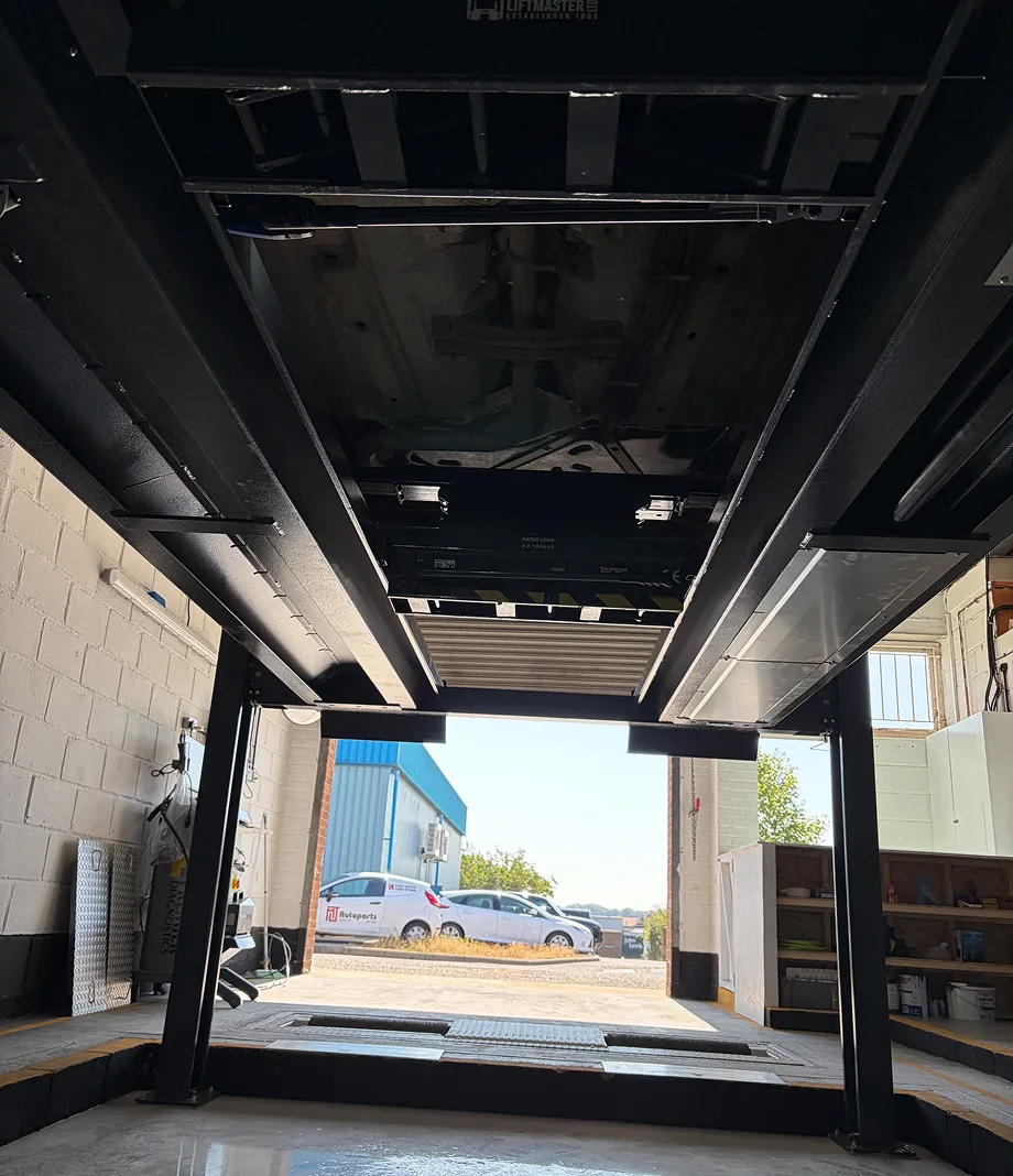 View from underneath a car raised on a workshop lift looking out through the open garage doors