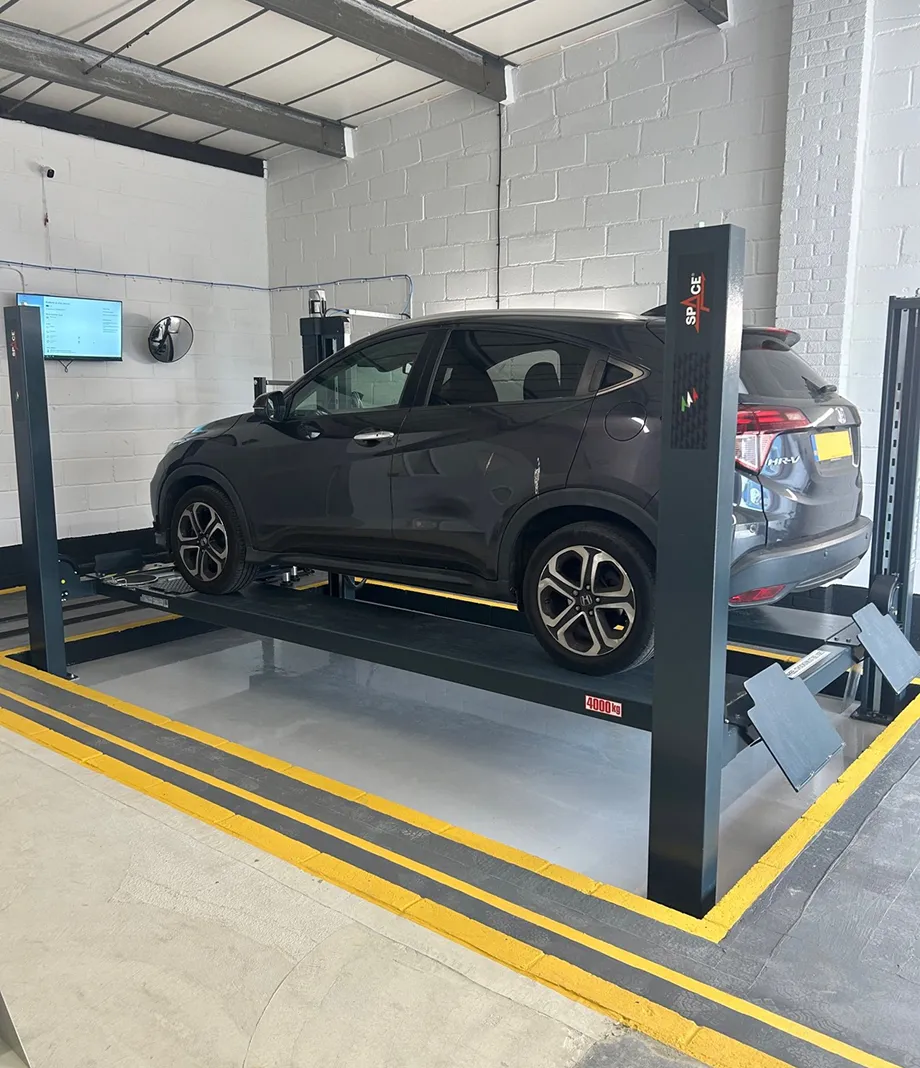 A dark grey Honda SUV raised on a four-post lift in the MOT bay