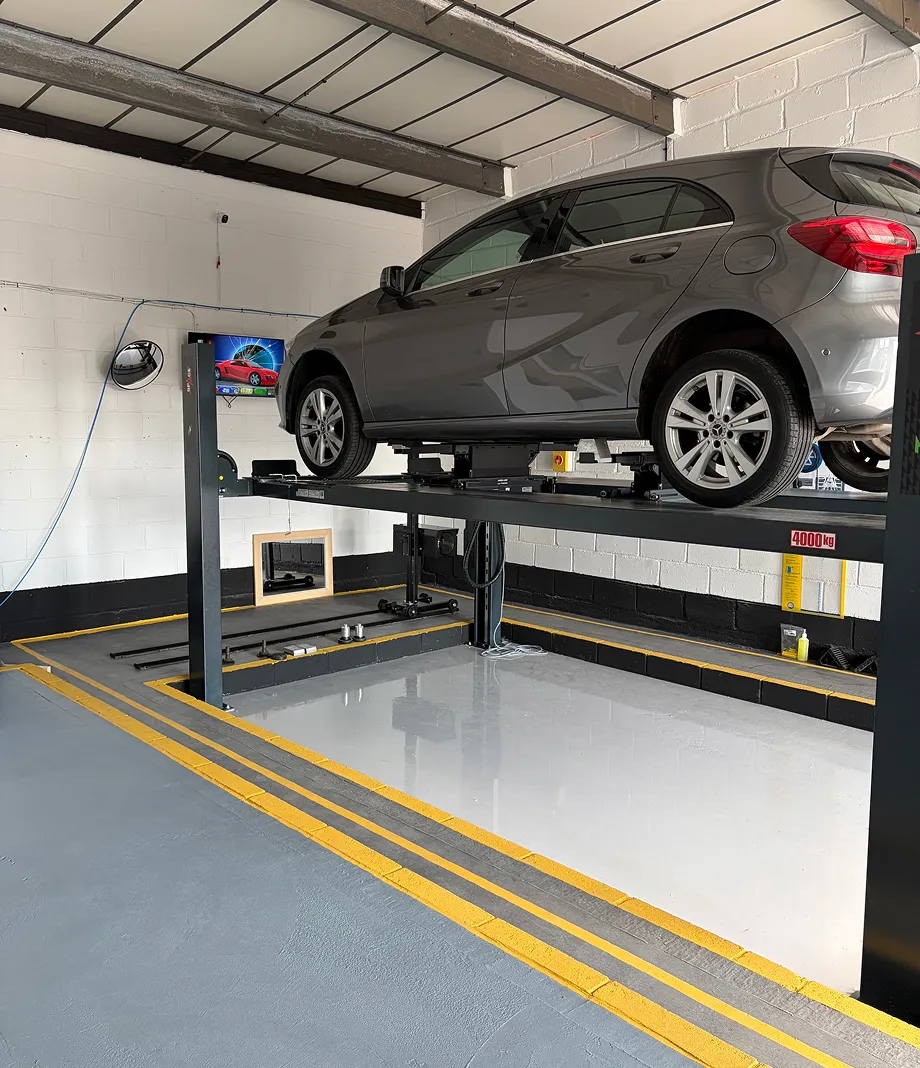 A grey Mercedes-Benz hatchback raised on a four-post lift in the workshop