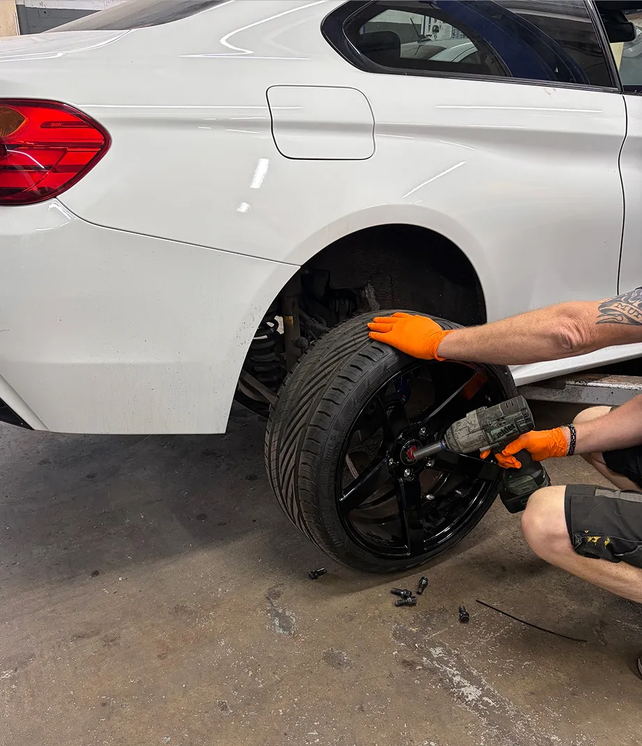 A mechanic using an impact wrench to work on a black alloy wheel